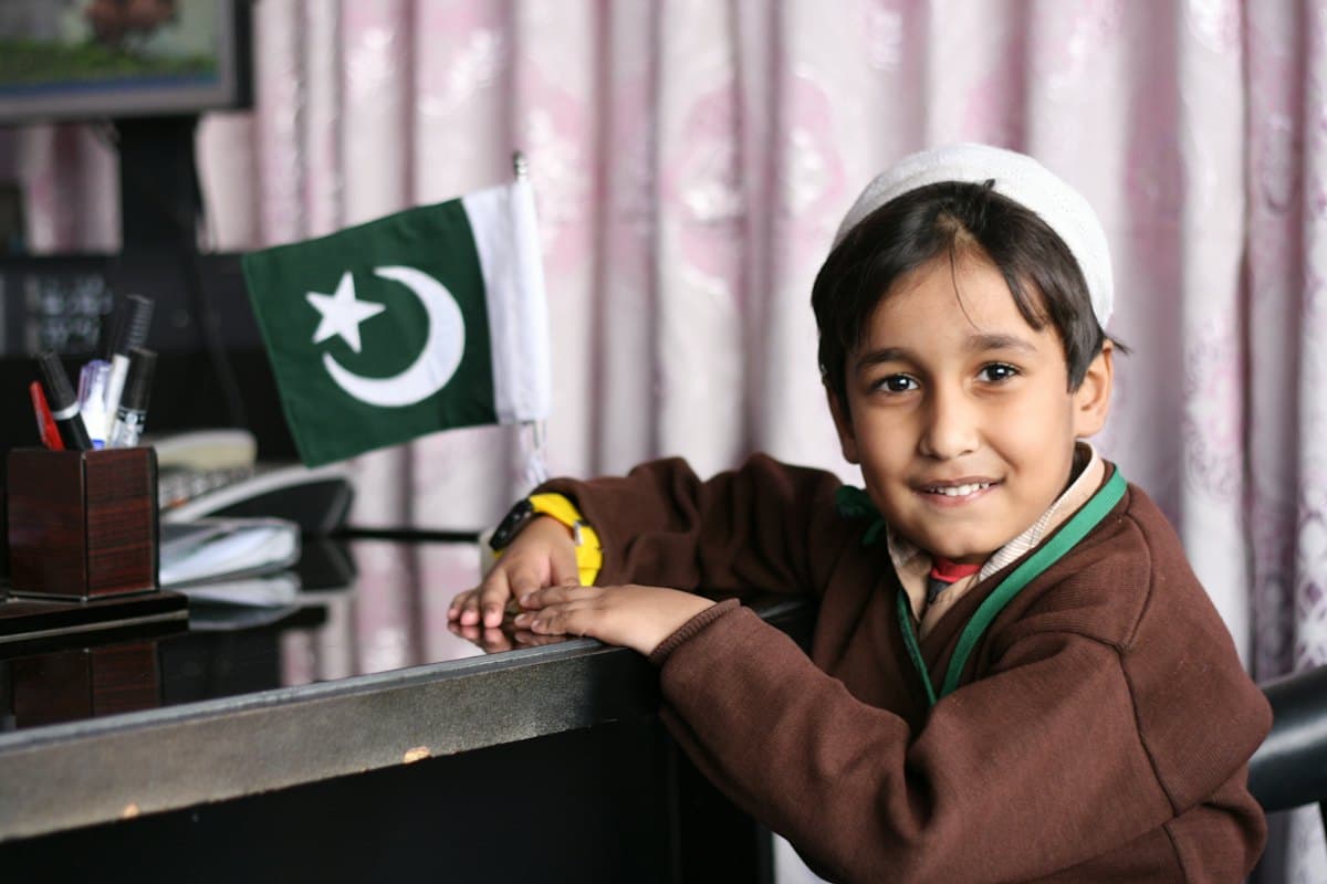 A smiling schoolgirl at her desk beside a small Pakistani flag