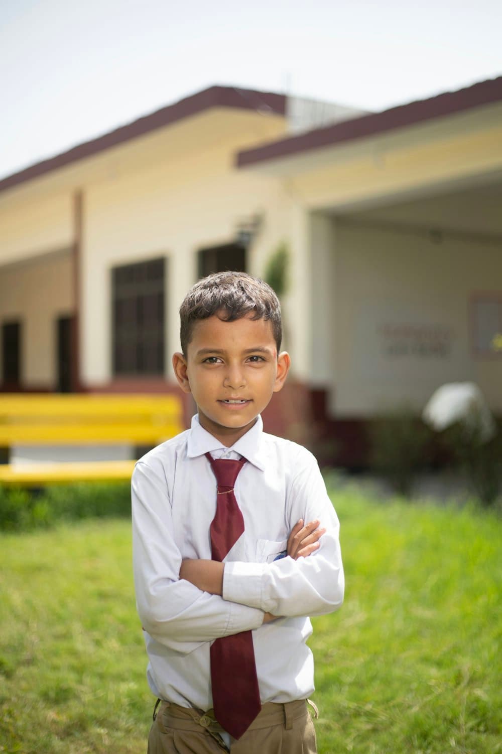 A young student in a white shirt and red tie standing on the school lawn
