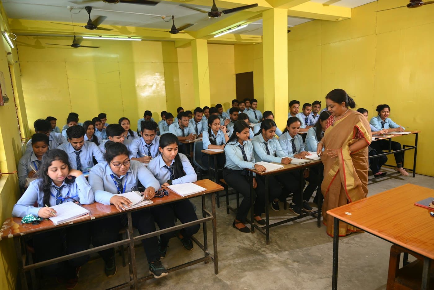 A teacher walking between rows of students working at their desks
